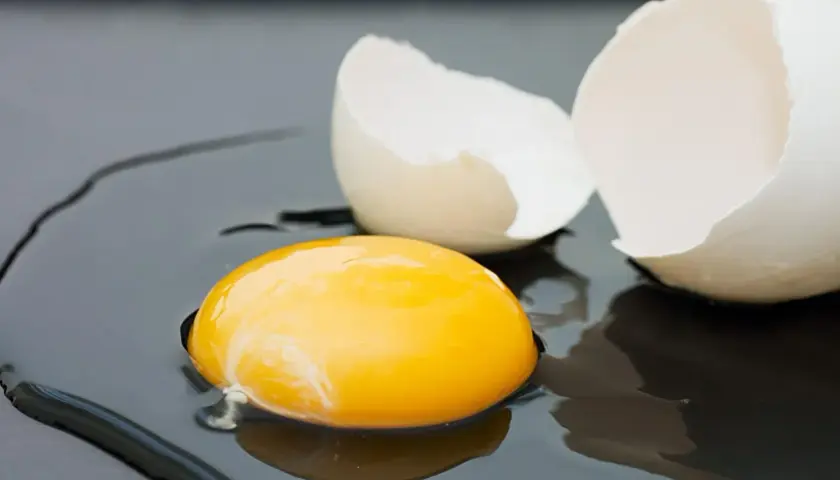 Rozbite jajko na ciemnym tle. Żółtko lśni, a skorupka czeka na usmażenie. Zastanawiasz się nad jajko smażone kcal?