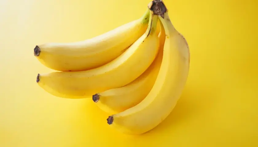 Pęczek żółtych bananów na żółtym tle. Zastanawiasz się, ile kalorii ma średni banan?
