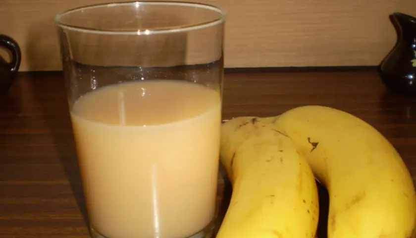 Szklanka orzeźwiającego soku z banana obok dwóch dojrzałych bananów. Idealny napój na szybkie śniadanie.