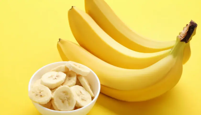 Pytanie: czy banany są kaloryczne? Na żółtym tle pęczek żółtych bananów i miseczka z plasterkami banana.