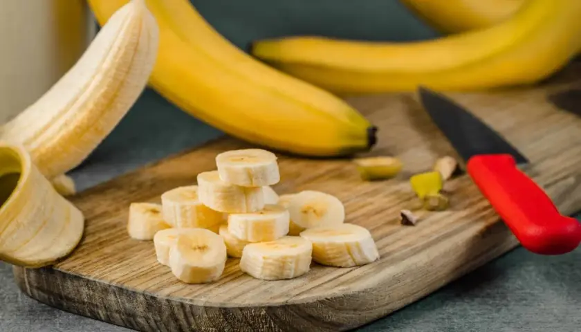 Plasterki banana na desce, idealne na pusty żołądek. Obok leży nóż z czerwoną rączką.