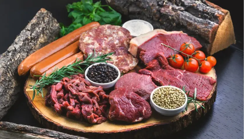 Mięso, kiełbaski, pomidorki i przyprawy na desce. Idealne składniki na dietę karniwora co jeść.