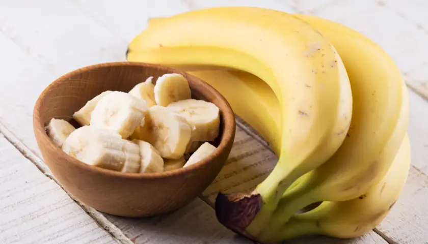 Dojrzały banan kcal w miseczce i pęczek bananów na drewnianym stole.