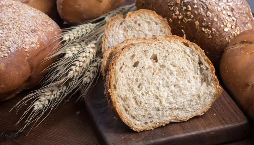 Różnorodne pieczywo, w tym bochenki z ziarnami i kromki chleba pełnoziarnistego. Idealne, gdy zastanawiasz się, jakie pieczywo przy odchudzaniu wybrać.