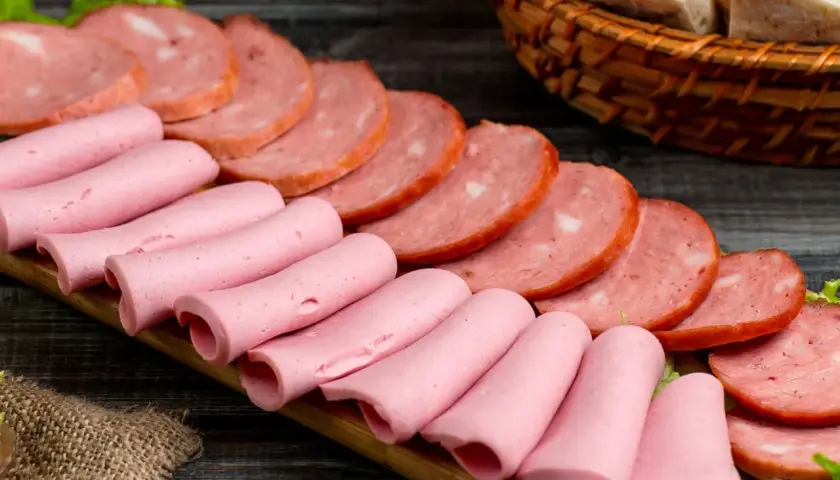 Na desce ułożone są różowe parówki i plastry wędliny. Zastanawiasz się, jakie wędliny są najzdrowsze?