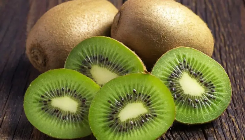 Kiwi na refluks. Dwa całe owoce kiwi i cztery przekrojone na pół, ukazujące zielony miąższ z czarnymi pestkami, leżą na drewnianym blacie.