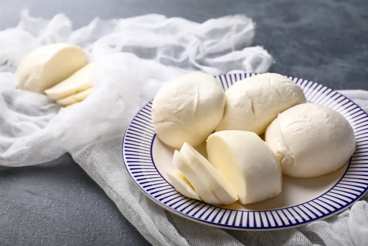 Świeża mozzarella na talerzu, pokrojona i w całości. Czy mozzarella podnosi cukier? Ten ser jest niskowęglowodanowy.