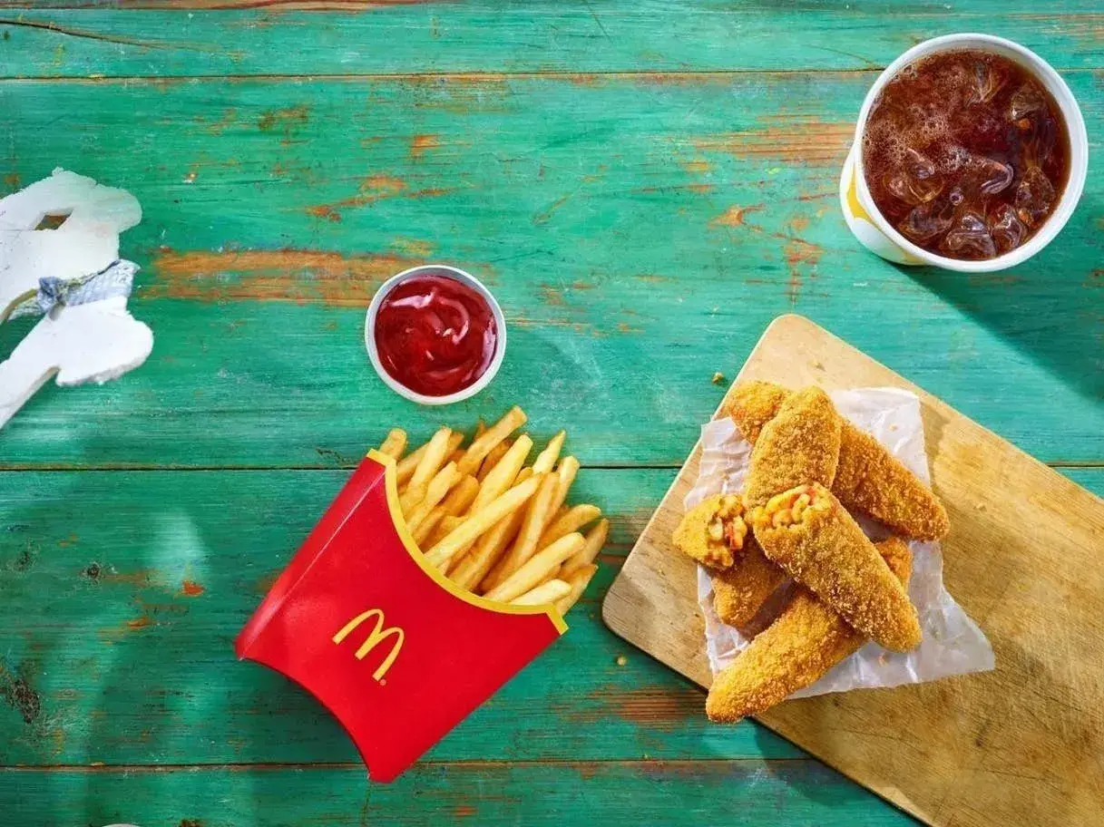 Chrupiące nuggetsy z serem i kukurydzą – to jest wege w maku! Obok frytki, ketchup i napój.