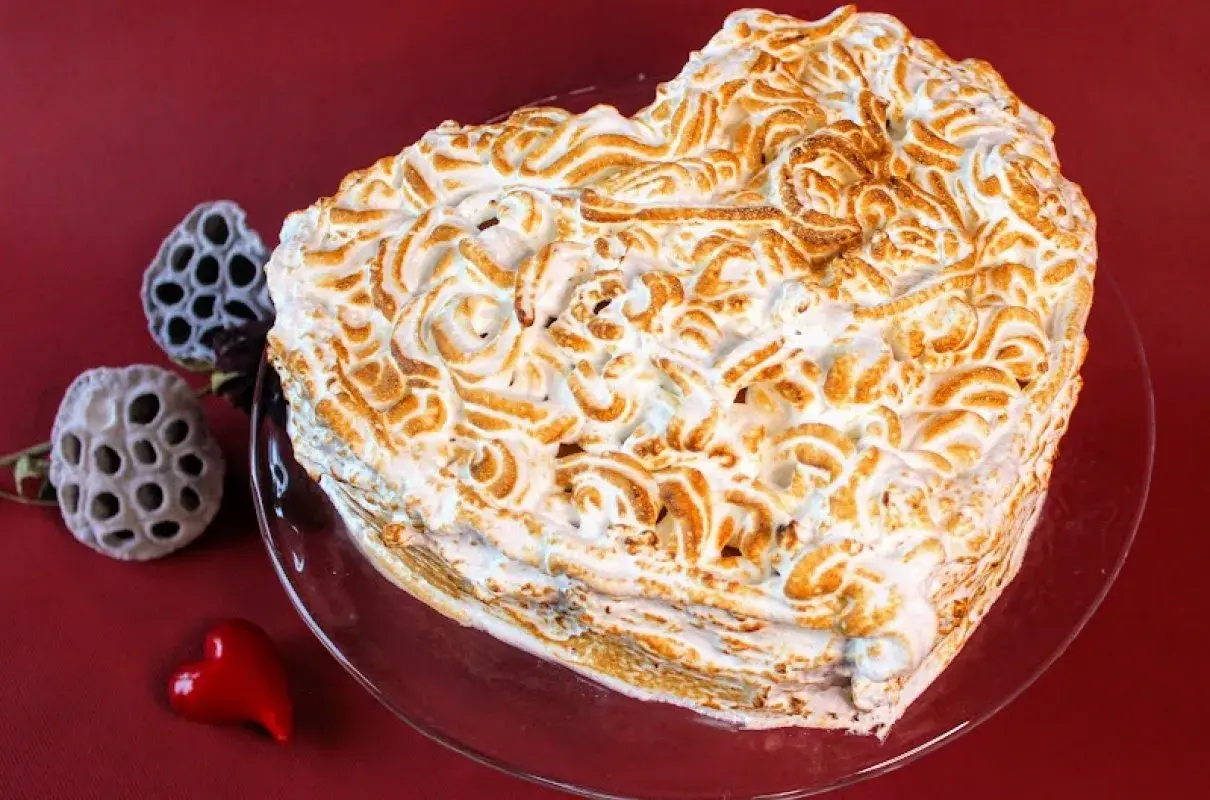 Serce z bezy, pyszne ciasto bez cholesterolu, ozdobione wzorami. Obok suszone kwiaty i czerwone serduszko.