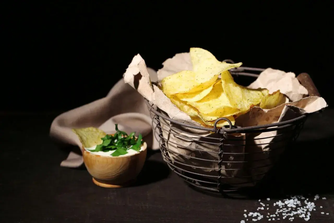 Koszyk pełen chipsów tortilla, obok miseczka z dipem i ziołami. Czy chipsy tortilla są zdrowe? To zależy od składników i sposobu przygotowania.