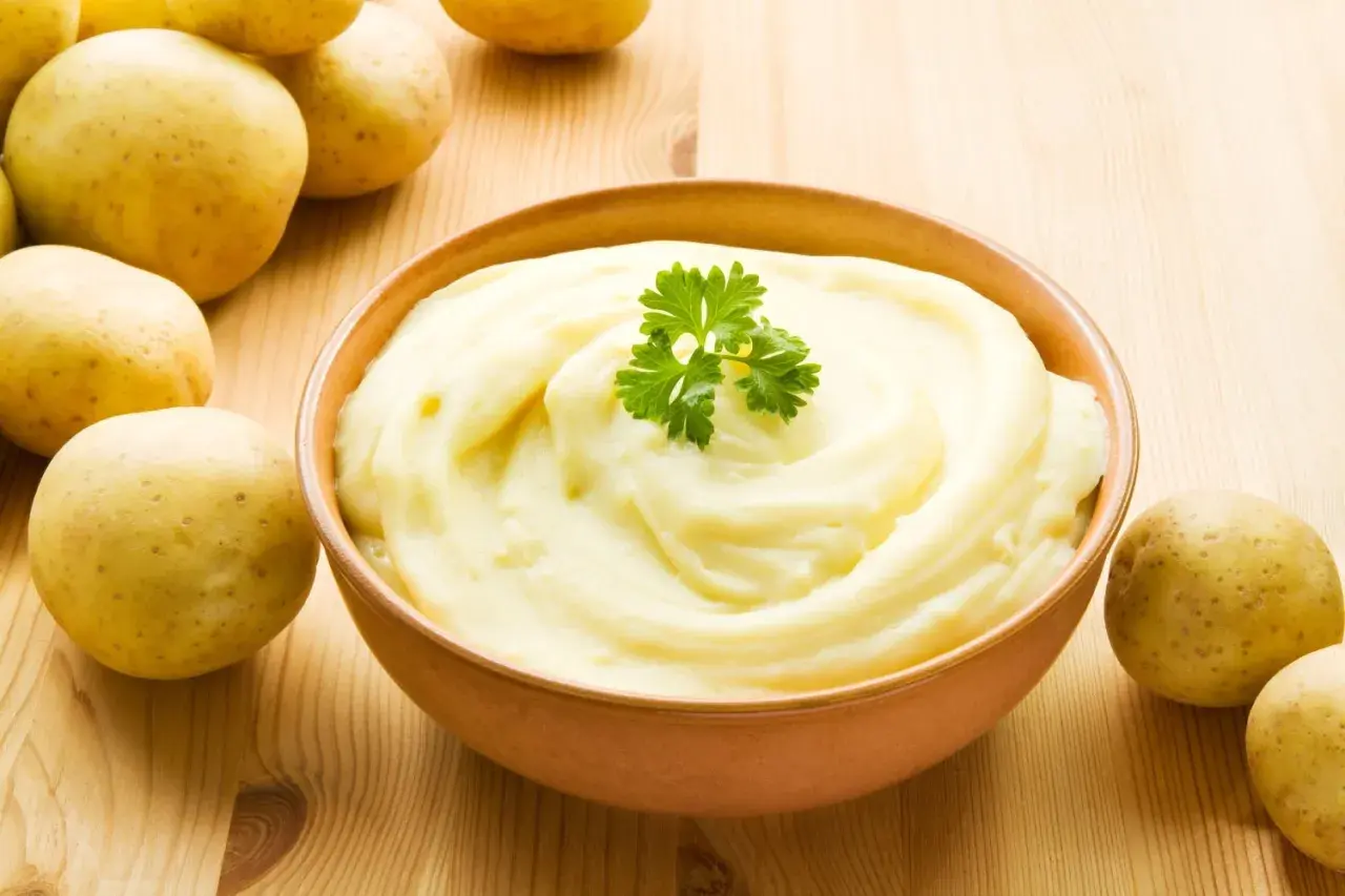Aksamitne puree ziemniaczane, ozdobione natką pietruszki, obok świeżych ziemniaków. Idealne jako dodatek do obiadu.