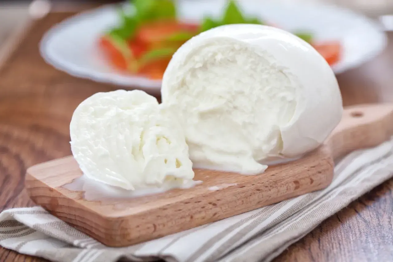 Świeża kulka mozzarelli na desce, w tle sałatka. Zastanawiasz się, ile kcal ma kulka mozzarelli?