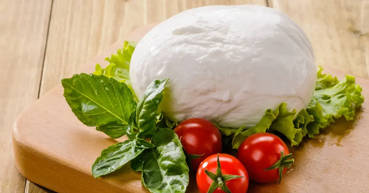 Kulista mozzarella, pomidorki i bazylia na desce. Czy mozzarella ma dużo białka? Tak, to świetne źródło białka!