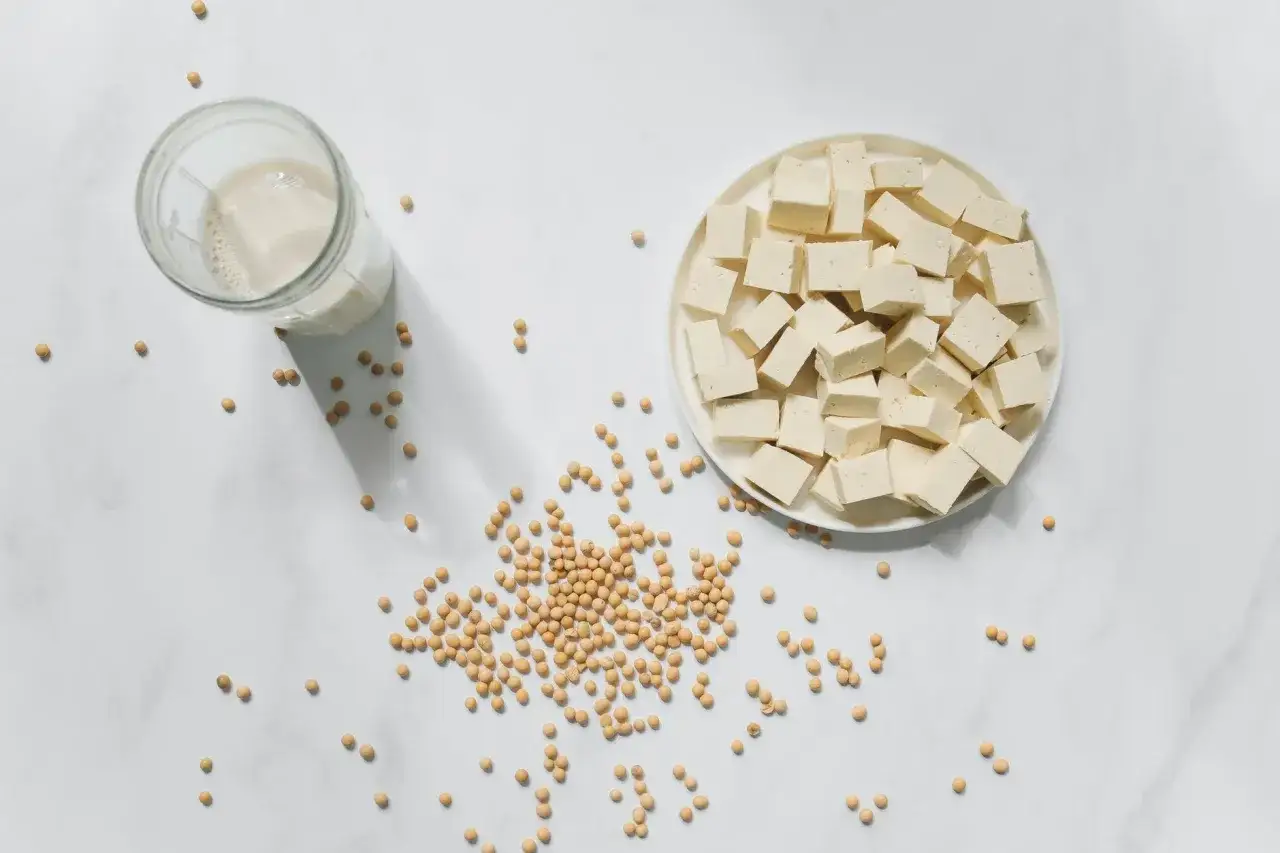 Kostki tofu na talerzu, obok szklanka mleka sojowego i ziarna soi. Czy tofu to nabiał? Nie, to produkt roślinny.