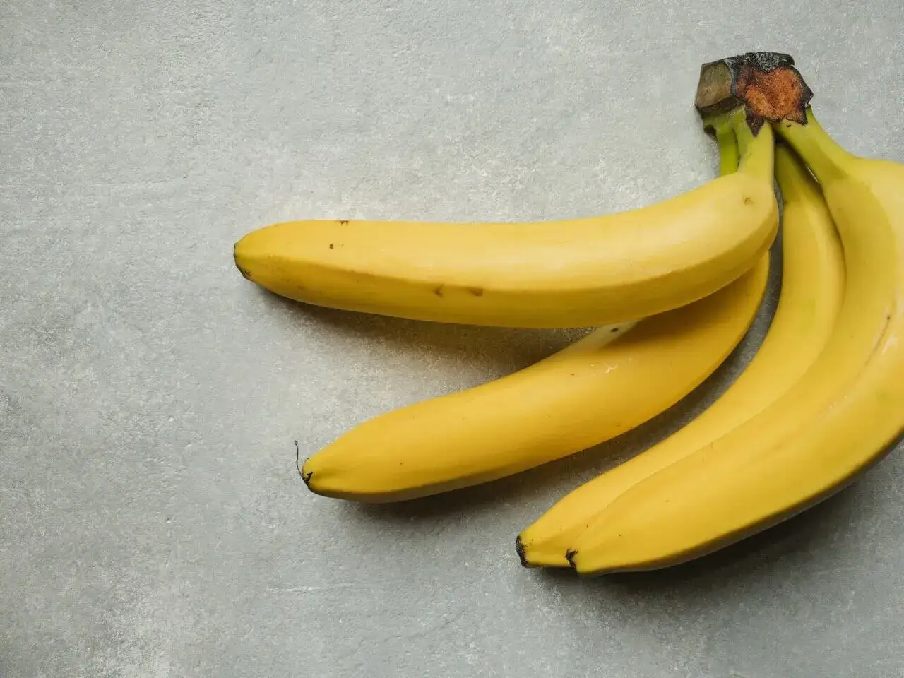 Kilka dojrzałych bananów leży na szarym tle. Duży banan to świetne źródło energii i błonnika, a jego kcal są idealne na przekąskę.