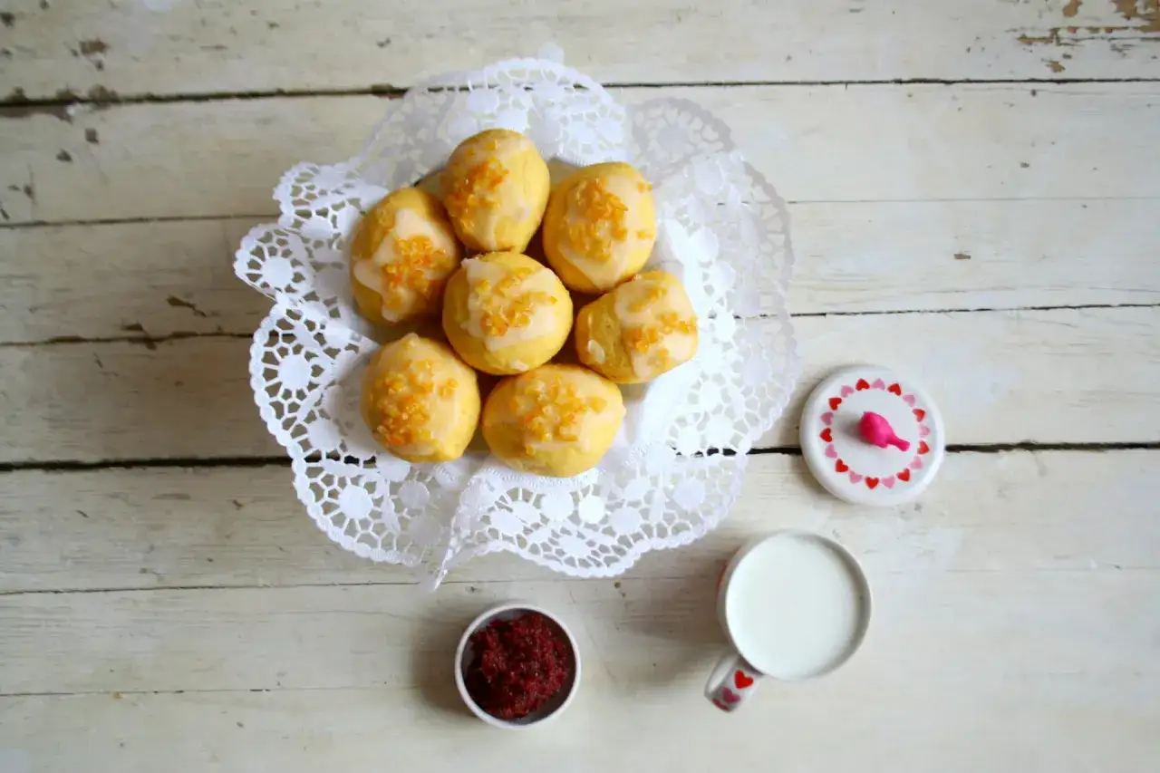 Pyszne paczki z batatow, polane lukrem i posypane kandyzowana skórka pomaranczowa, obok kubek mleka i mala miseczka z dzemem.