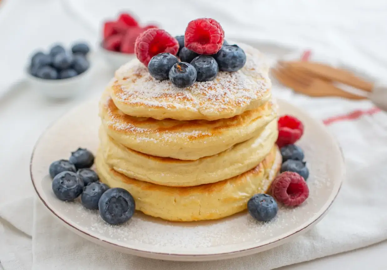 Stos puszystych pancakes z jagodami i malinami, posypane cukrem pudrem. Czy pancakes są lekkostrawne? Zależy od składników!