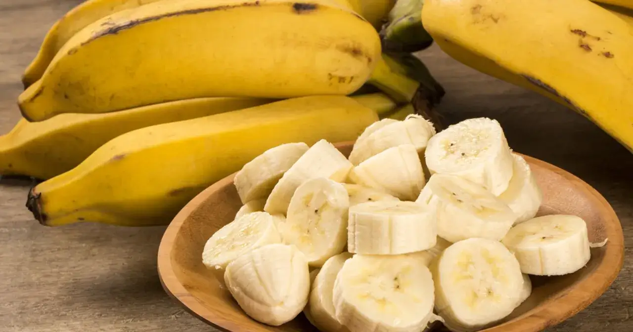 Bananów na drewnianym stole, część pokrojona w plasterki. Dowiedz się, ile błonnika ma banan.