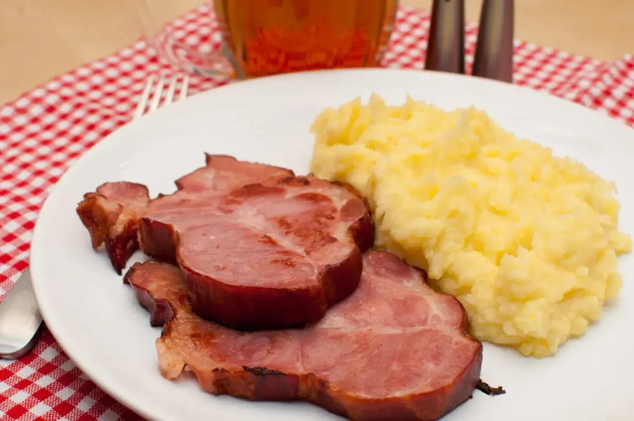 Jak zrobić idealne purée ziemniaczane? Dodaj jeden składnik, a uzyskasz kremową konsystencję. Na talerzu obok purée leżą plastry wędzonego mięsa.