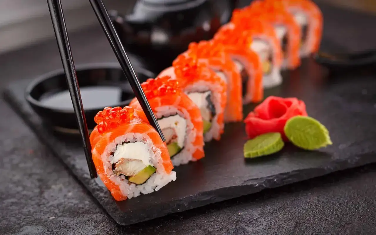Chopsticks podnoszą rolkę sushi z łososiem i ikrą. Idealne sushi na diecie, z awokado i serkiem.