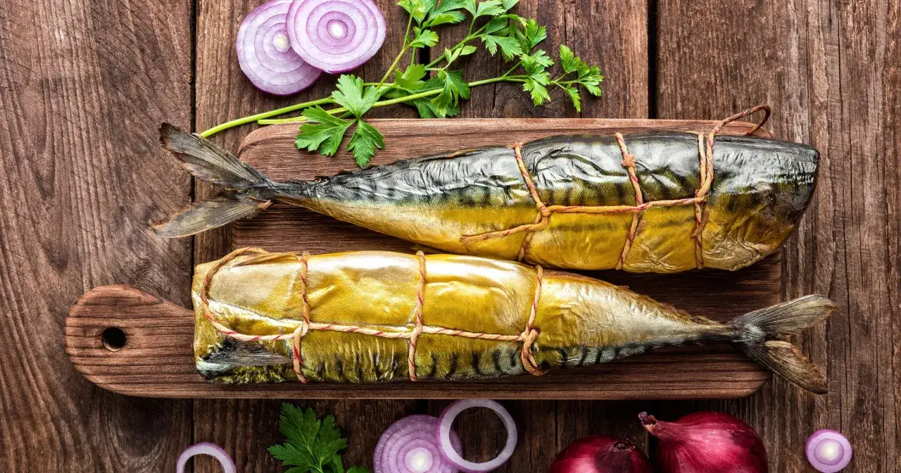 Dwie wędzone makrele na desce, obok cebuli i natki. Czy makrela jest zdrowa? Tak, to bogactwo kwasów omega-3!