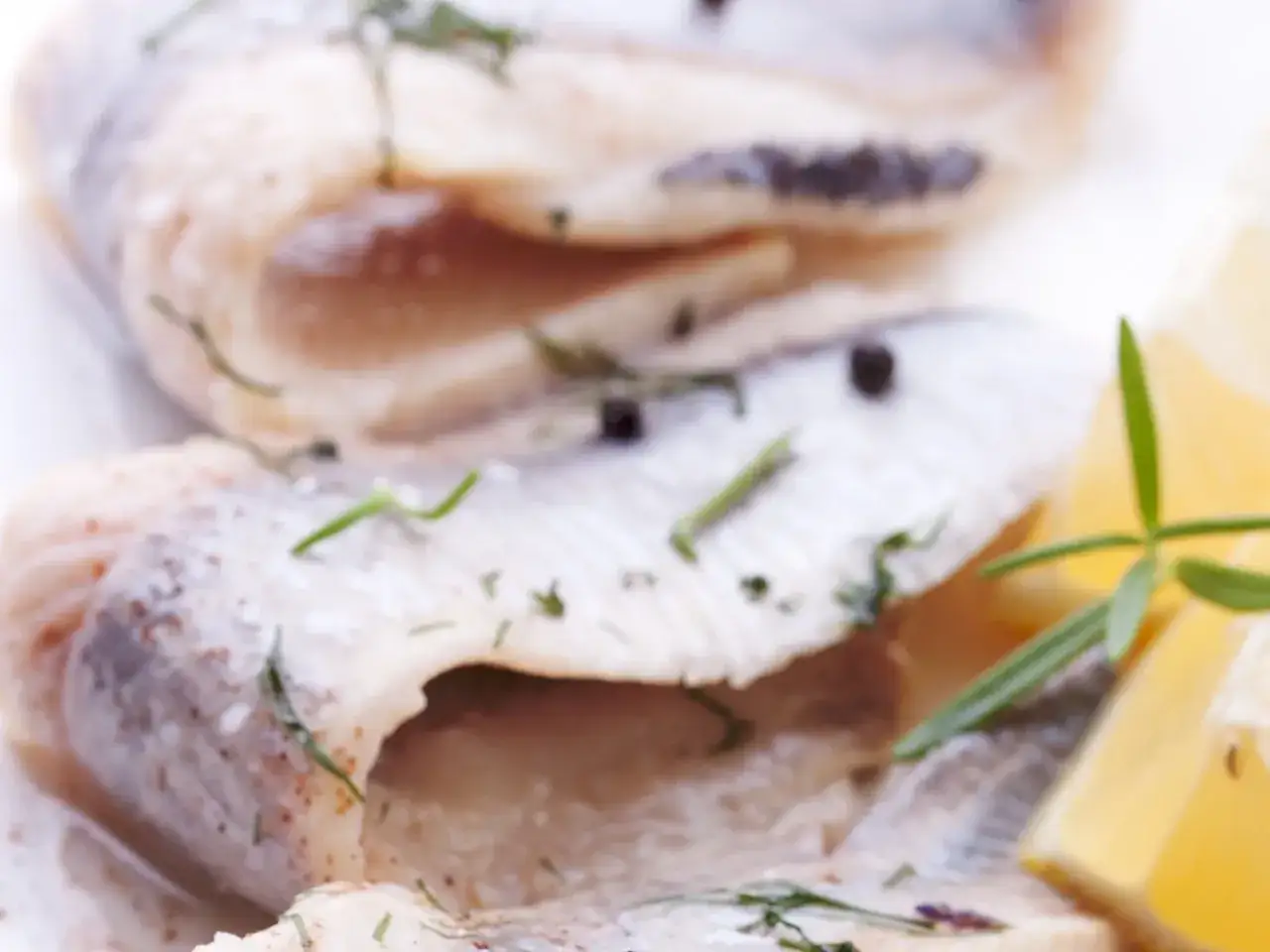 Filety śledziowe z koperkiem i pieprzem, obok plasterki cytryny. Czy śledzie solone są zdrowe? Tak, to źródło omega-3.