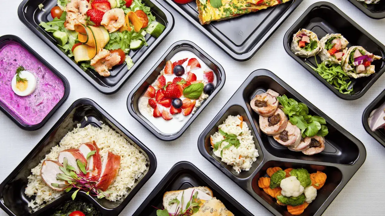 Różnorodne dania z cateringu dietetycznego Wieluń: sałatka z krewetkami, jogurt z owocami, ryż z kurczakiem, warzywa i mięso.