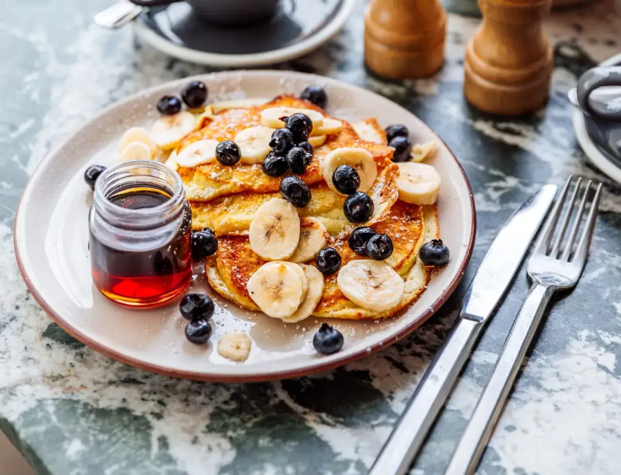 Pancakes z bananem i borówkami, posypane cukrem pudrem, z syropem klonowym. Czy pancake są zdrowe? Z owocami i bez nadmiaru syropu, mogą być!