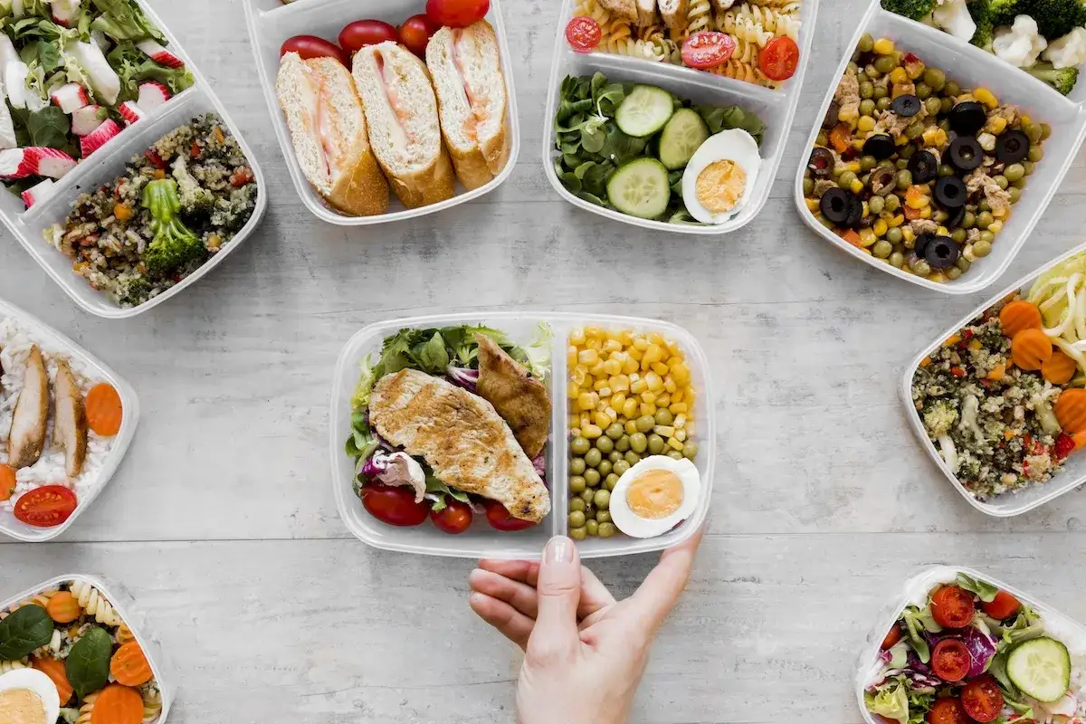Jakie są opcje menu w cateringu imprezowym? Różnorodne dania w pojemnikach: sałatki, kanapki, kurczak z warzywami, makaron, ryż.