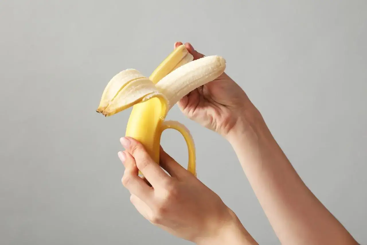 Dłonie obierają dojrzałego banana. Czy banan jest lekkostrawny? Tak, to świetna przekąska.