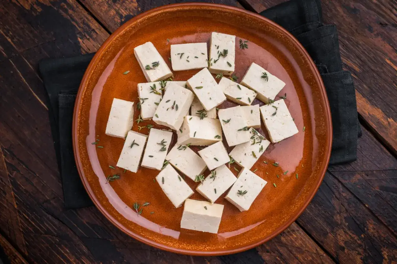 Pokrojone w kostkę tofu, posypane ziołami, na brązowym talerzu. Tak powstaje tofu, wszechstronny składnik kuchni roślinnej.