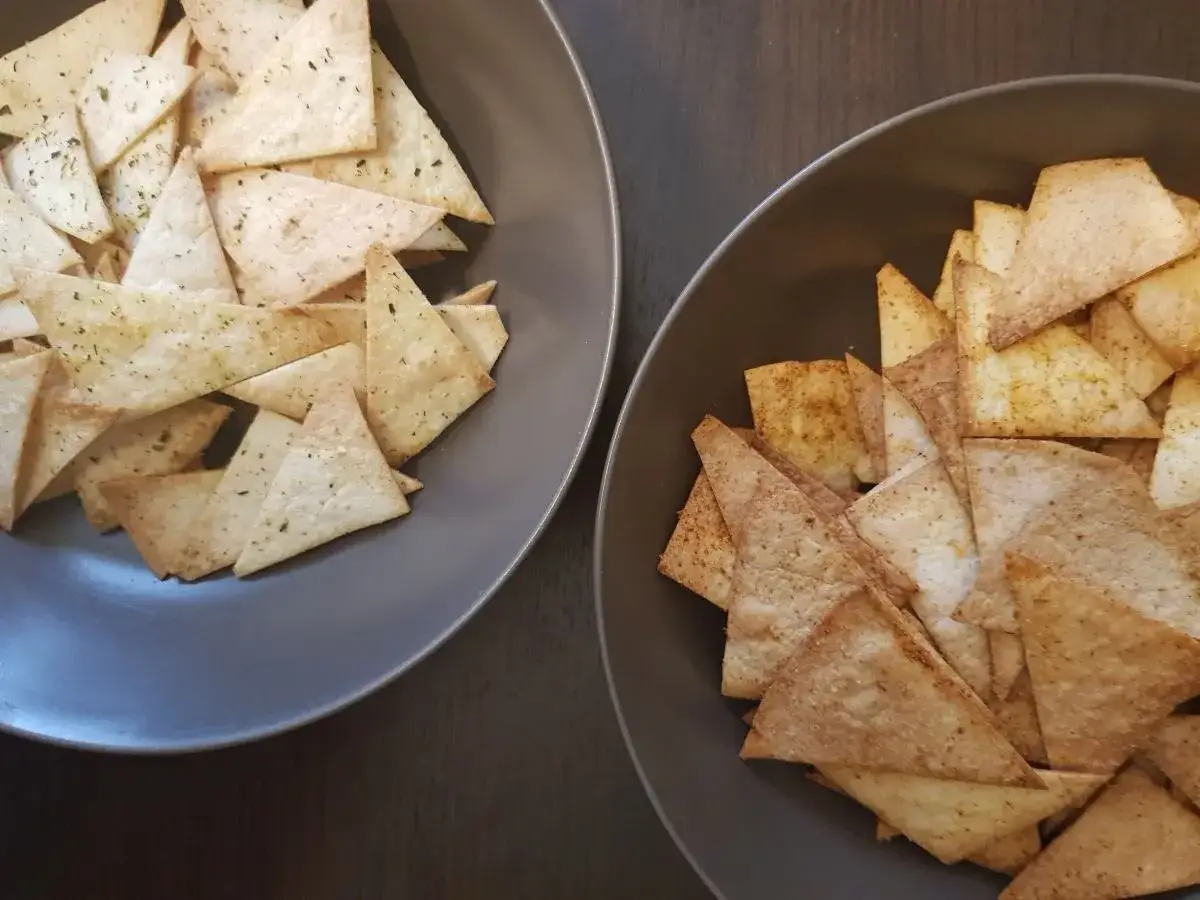 Dwa talerze pełne chrupiących chipsów tortilla, jeden z ziołami, drugi z przyprawami. Czy chipsy tortilla są zdrowe? To zależy od sposobu przygotowania!