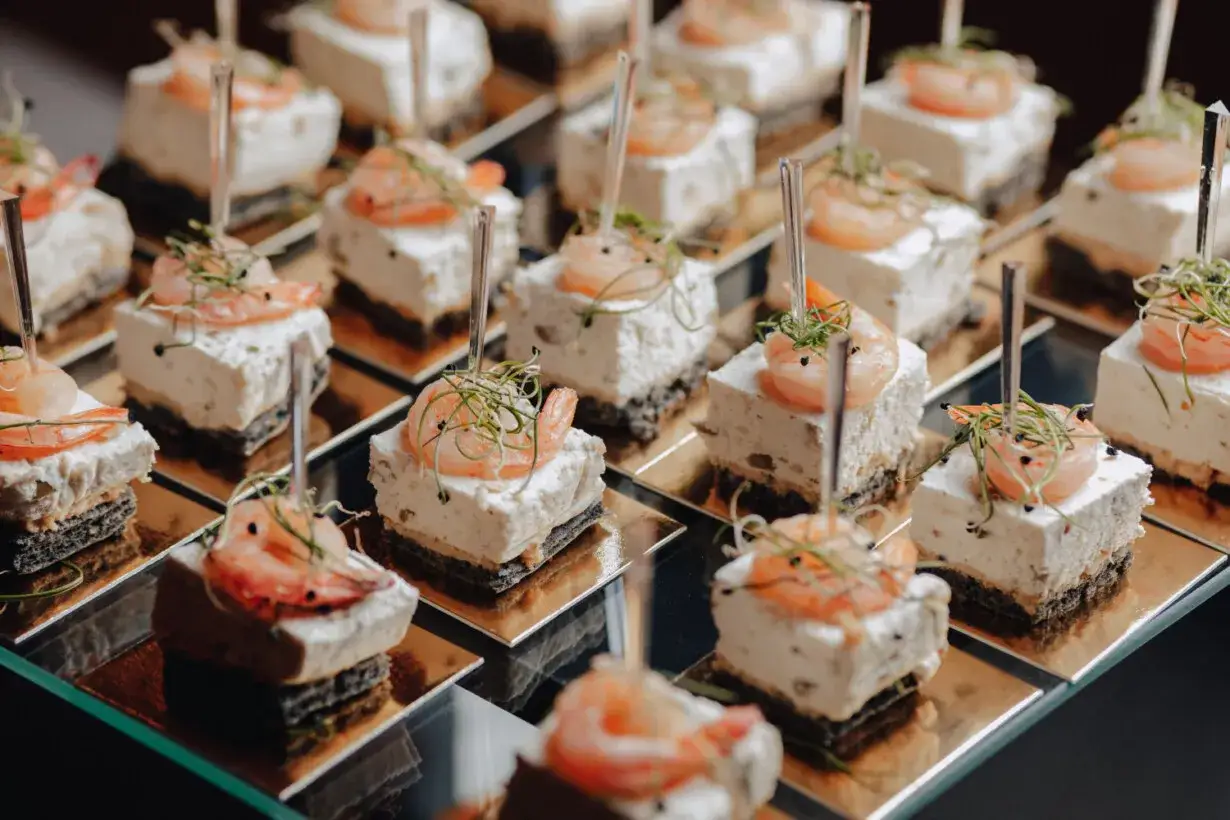 Krewetki na kremowym musie z ziołami, ułożone na czarnym spodzie. Tak działa catering – eleganckie przekąski na złotej podstawce.