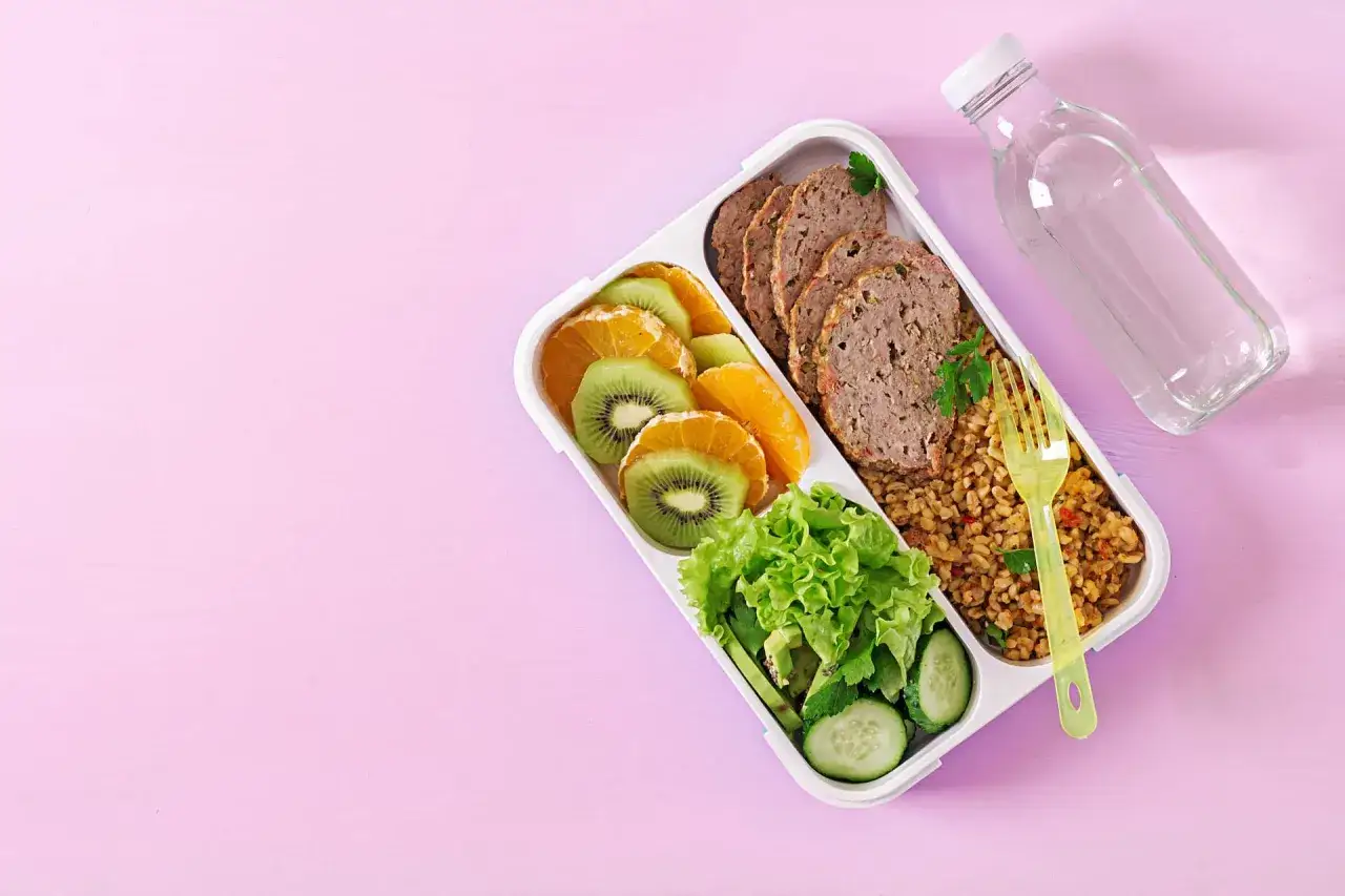 Zdrowy lunchbox z pieczonym mięsem, kaszą, sałatką i owocami. Idealne wysokobiałkowe posiłki do pracy.