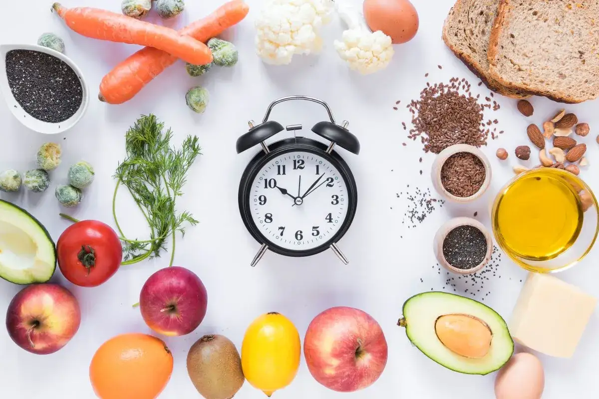 Zegar i zdrowe produkty: marchew, jabłka, awokado, pomidor, cytryna, kiwi, jajko, chleb, orzechy, nasiona chia, siemię lniane, oliwa, ser. Okno żywieniowe co jeść.