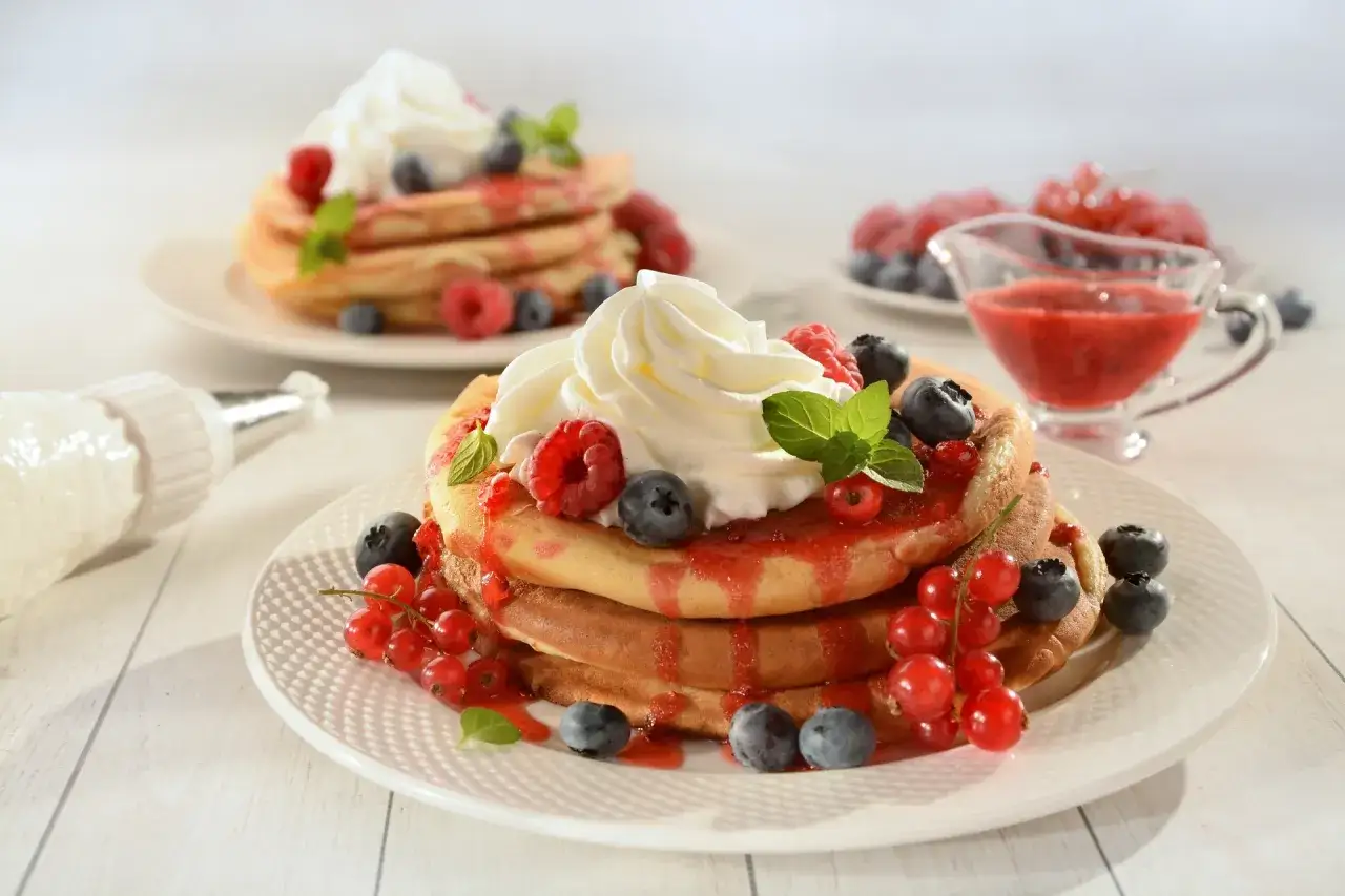 Stos owocowych naleśników z bitą śmietaną i jagodami. Czy pancake są zdrowe? Z owocami i bez dodatków, mogą być!