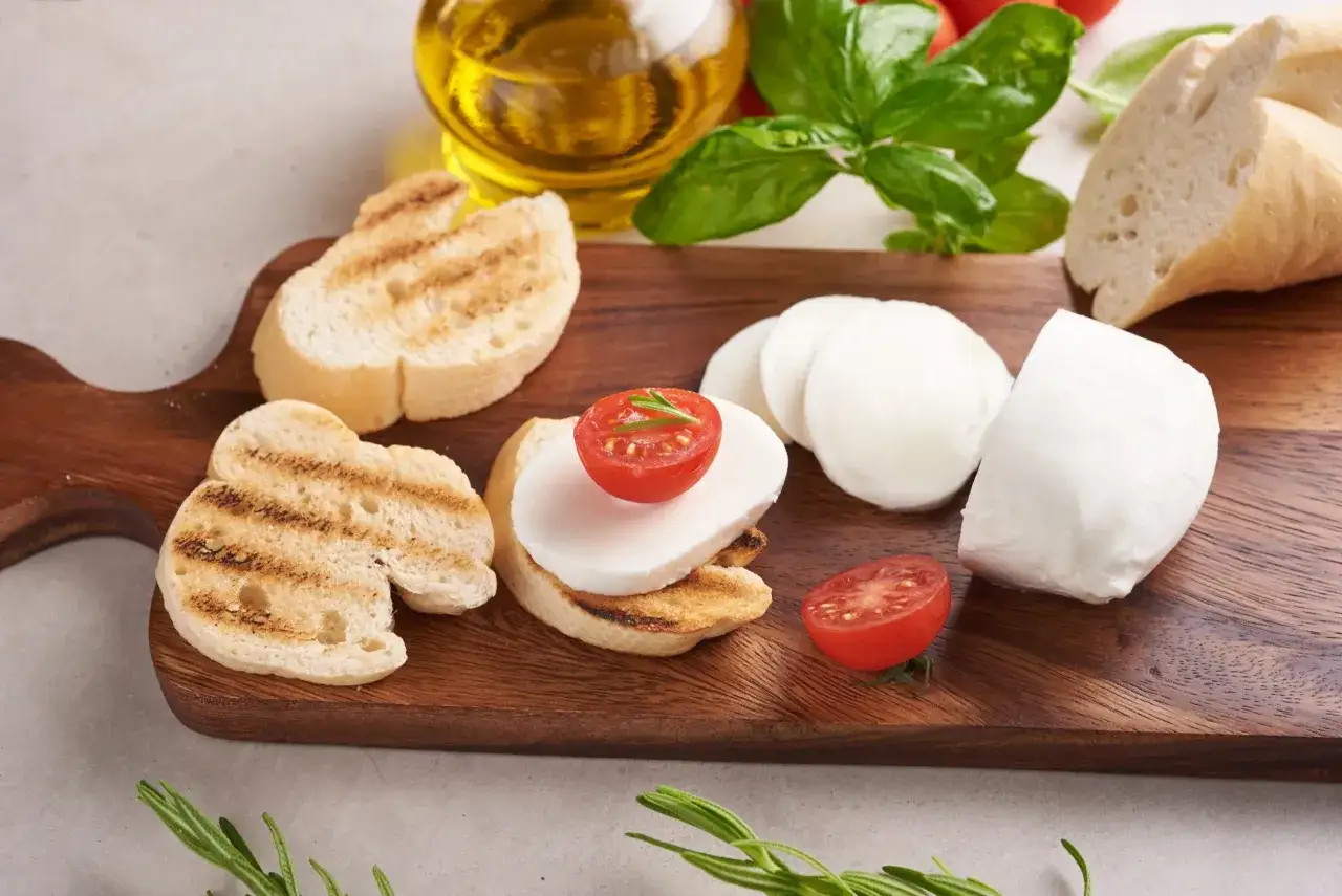 Na desce drewnianej grzanki z mozzarellą i pomidorkami. Czy mozzarella jest kaloryczna? Zależy od jej rodzaju, ale ta wygląda apetycznie!