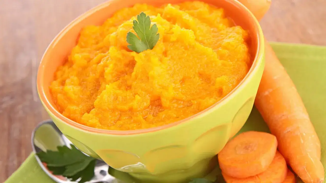 Pyszne puree z marchewki w miseczce, obok świeże marchewki. Dowiedz się, jak długo gotować marchew, by uzyskać idealną konsystencję.
