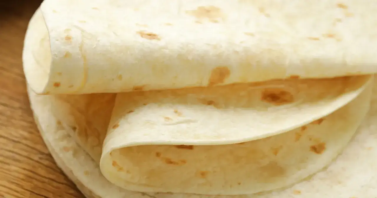 Stos cienkich placków tortilli na drewnianym blacie. Czy tortilla jest zdrowsza od chleba? Zależy od składników i sposobu przygotowania.