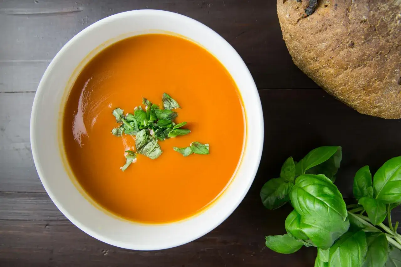 Pomidorowa zupa krem, idealna na dietę lekkostrawną. Warzywa i świeża bazylia tworzą pyszne danie. Obok kromka chleba.