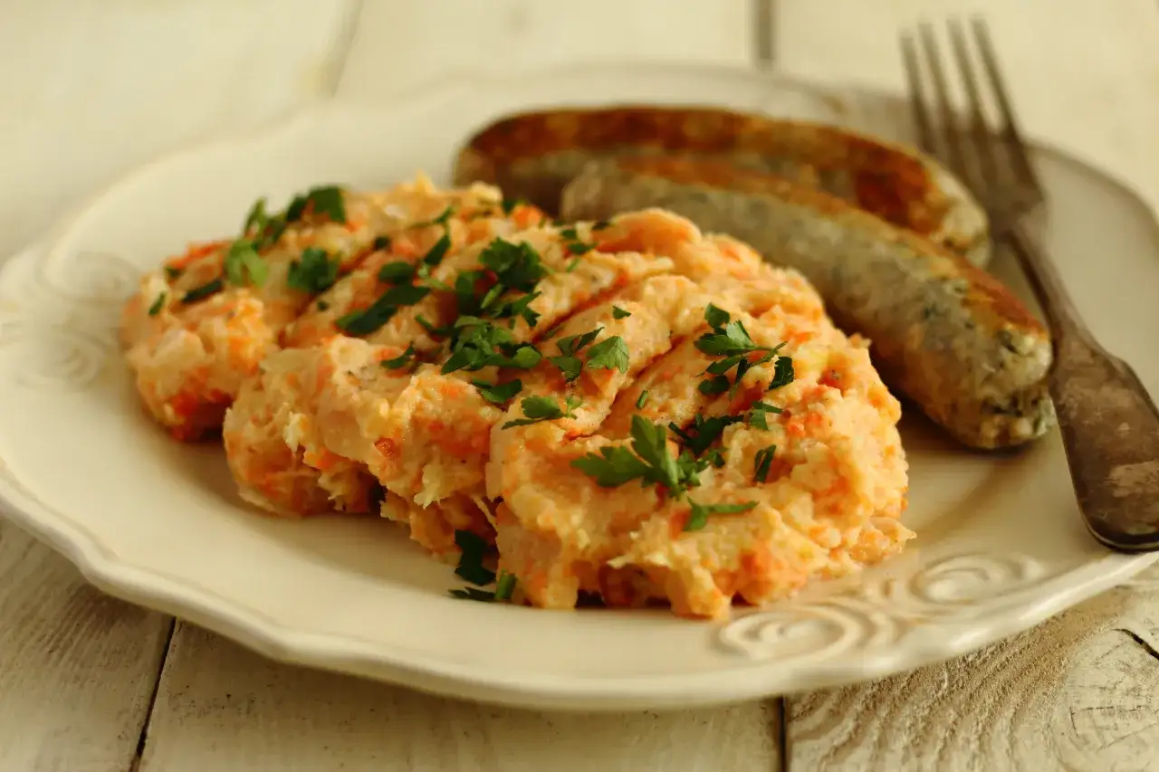 Pomarańczowe puree z marchewki i ziemniaków, posypane natką pietruszki, podane z kiełbaskami. Pyszne i zdrowe danie.