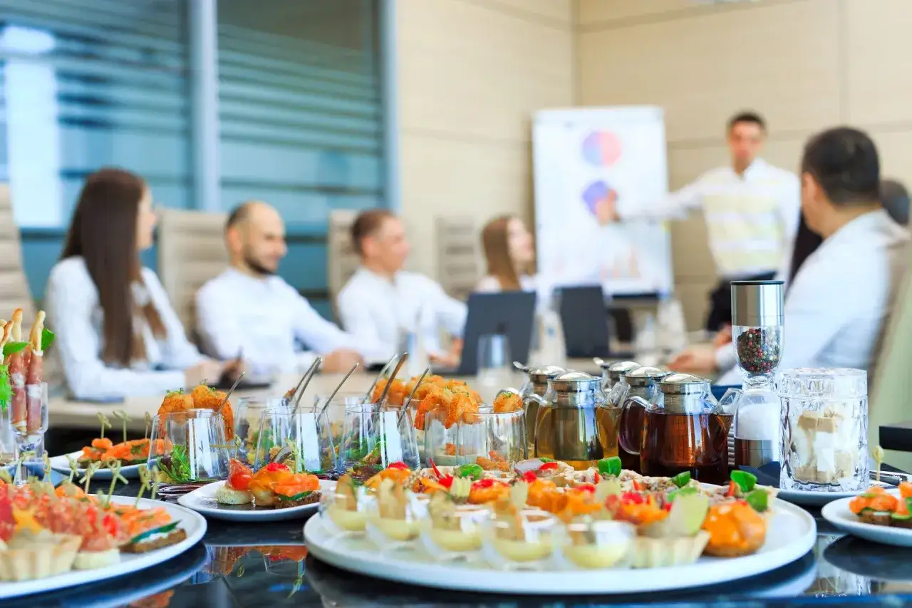 Eleganckie przekąski na stole, ludzie na spotkaniu biznesowym. Zastanawiasz się, ile kosztuje catering firmowy?