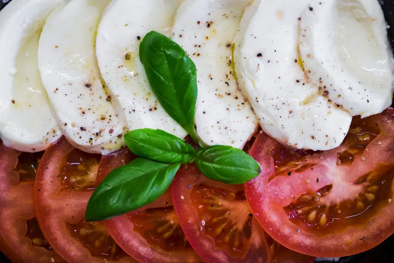 Plastry pomidorów i mozzarelli, skropione oliwą i posypane pieprzem. Czy ser mozzarella jest tłusty? Ten wygląda na wilgotny i kremowy.